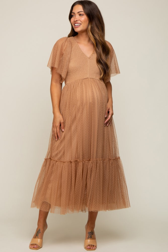 woman wearing a tan maternity dress with flutter sleeves and a tiered skirt, showing her baby bump