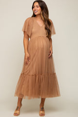 woman wearing a tan maternity dress with flutter sleeves and a tiered skirt, showing her baby bump