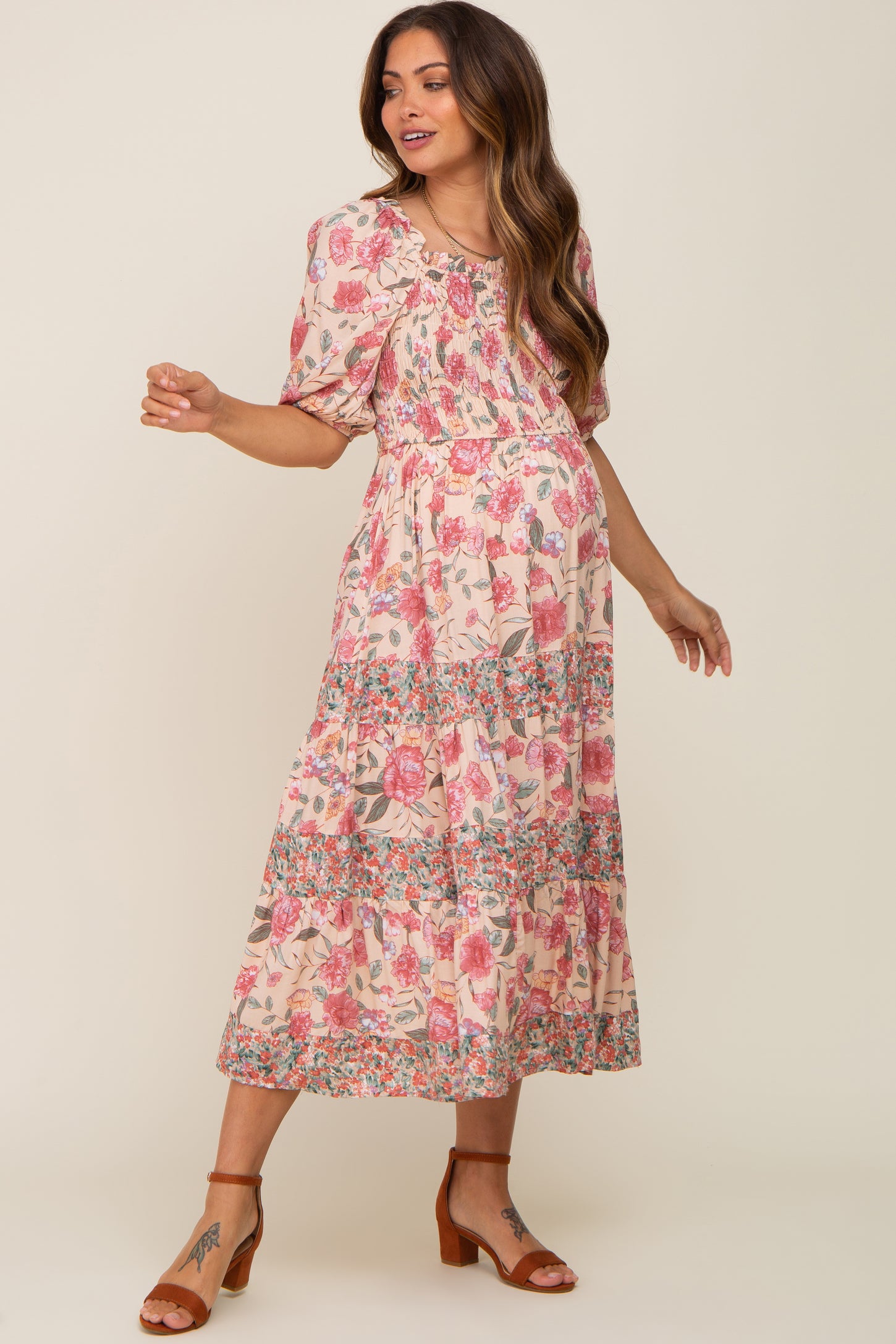 Pregnant woman wearing a pink floral smocked maternity midi dress with puff sleeves and brown block heel sandals