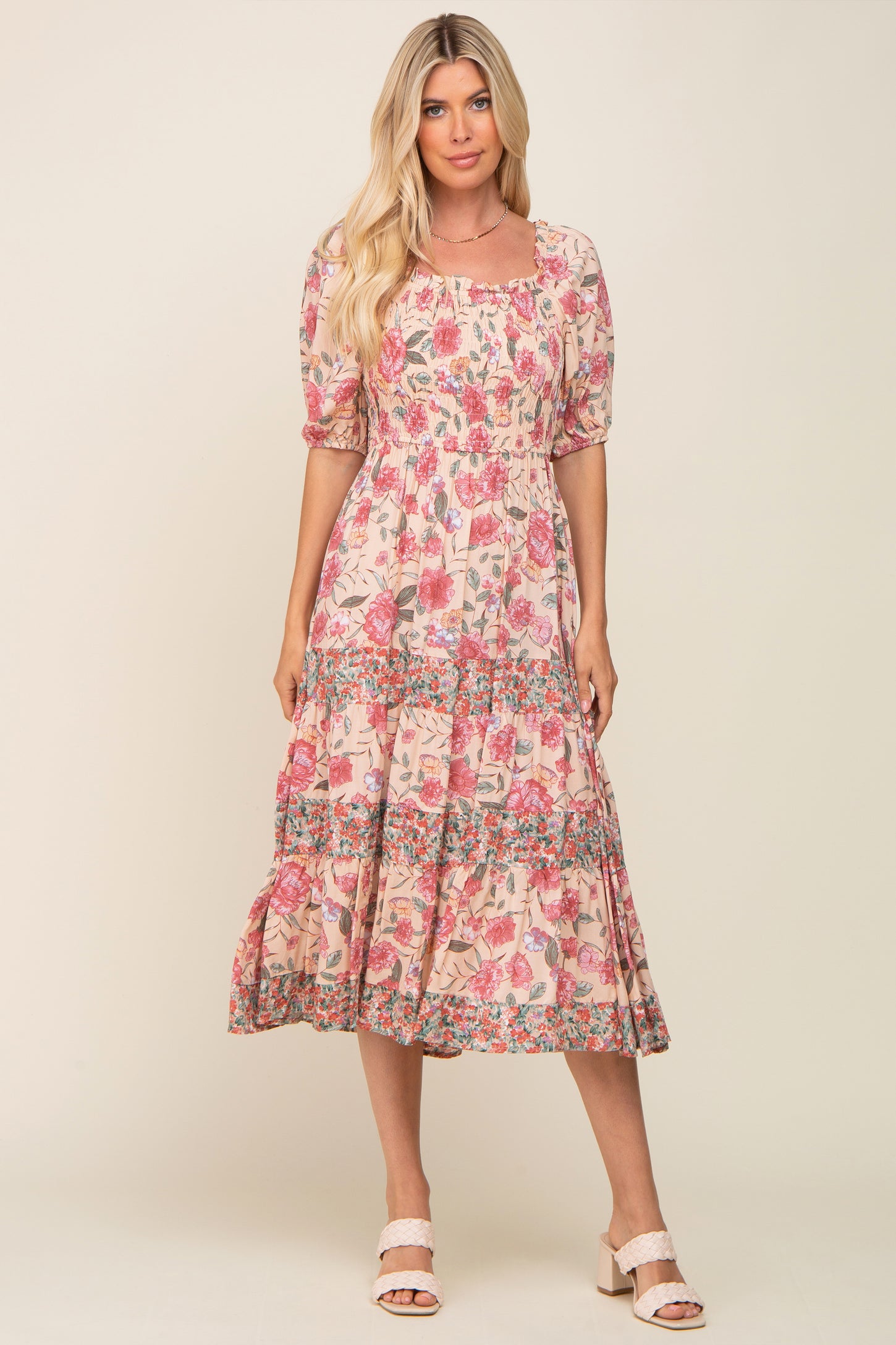 Woman wearing a pink floral smocked midi dress with puff sleeves and tiered skirt