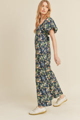 woman wearing a navy blue floral print wide leg jumpsuit and white sneakers against a neutral background
