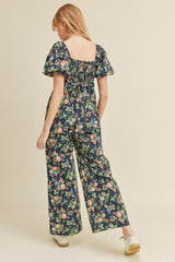 woman wearing a navy blue floral jumpsuit with short puff sleeves and a tie at the back