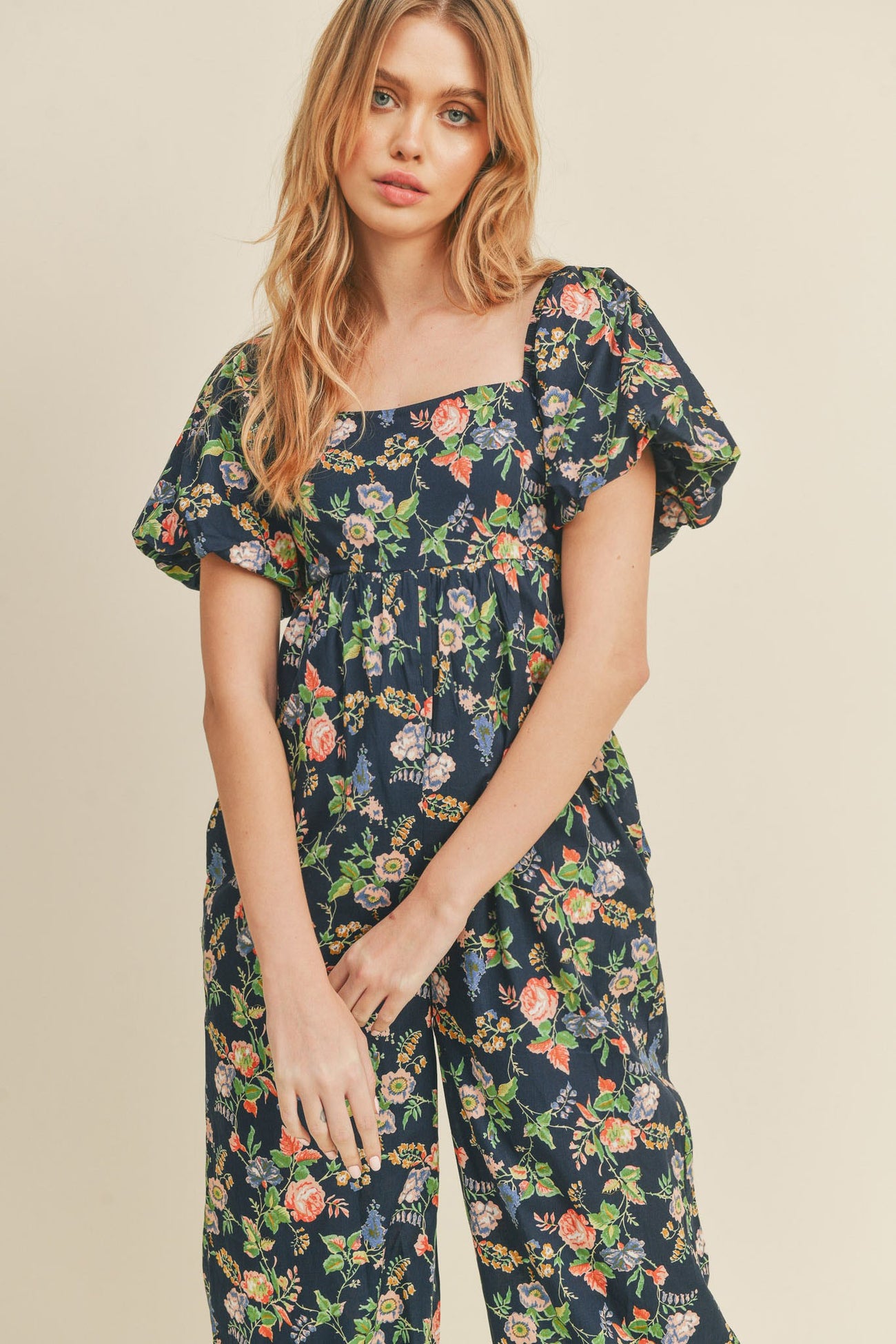 woman wearing a navy floral jumpsuit with a square neckline and puff sleeves