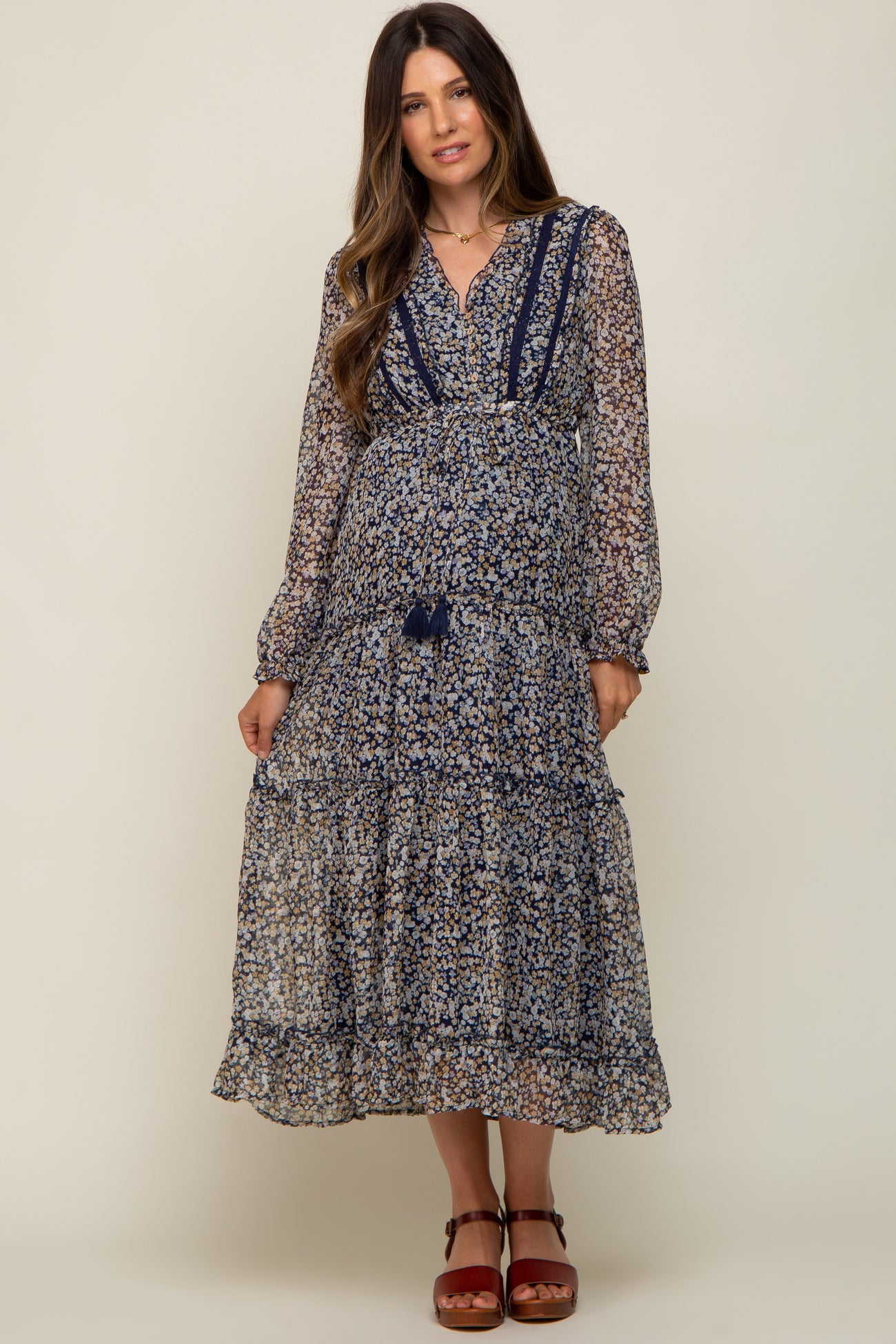 woman wearing a navy blue floral long sleeve maternity midi dress with tiered skirt and tassel tie