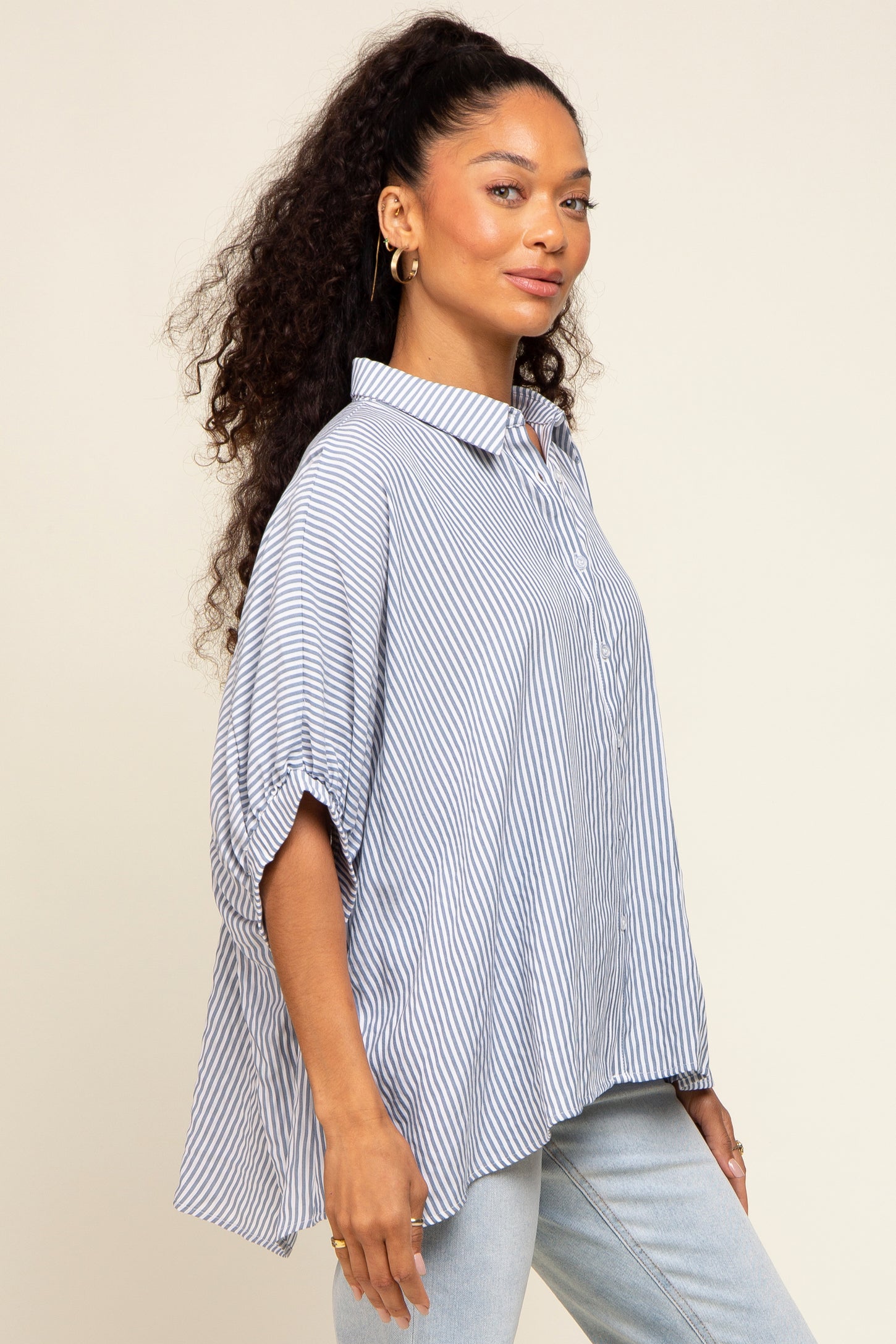 woman wearing a blue and white striped oversized button-down shirt and light wash jeans