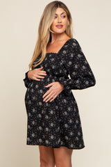 pregnant woman wearing a black floral smocked maternity dress with long sleeves, holding her baby bump