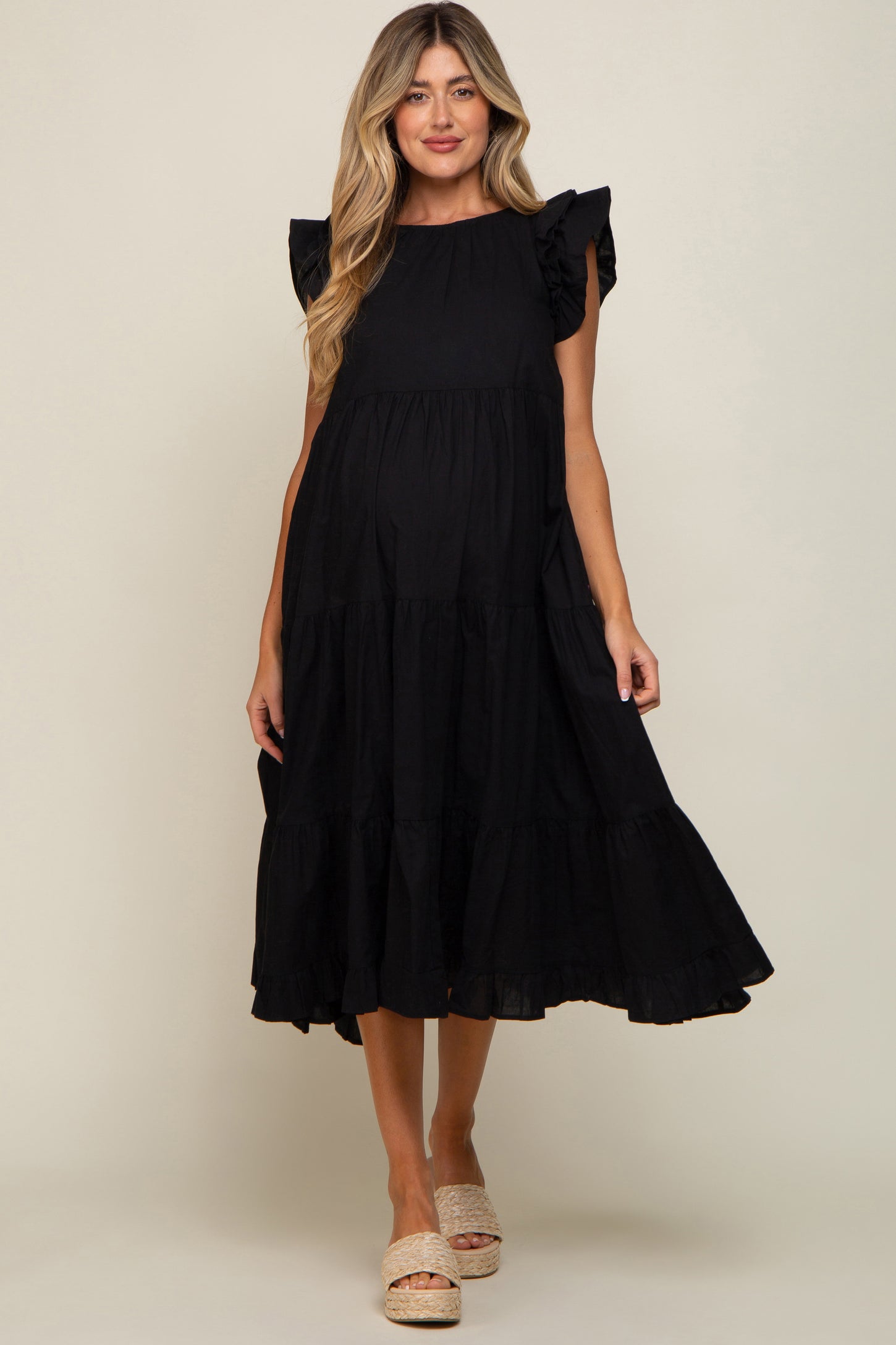 woman wearing a black tiered maternity midi dress with ruffle sleeves and woven platform sandals