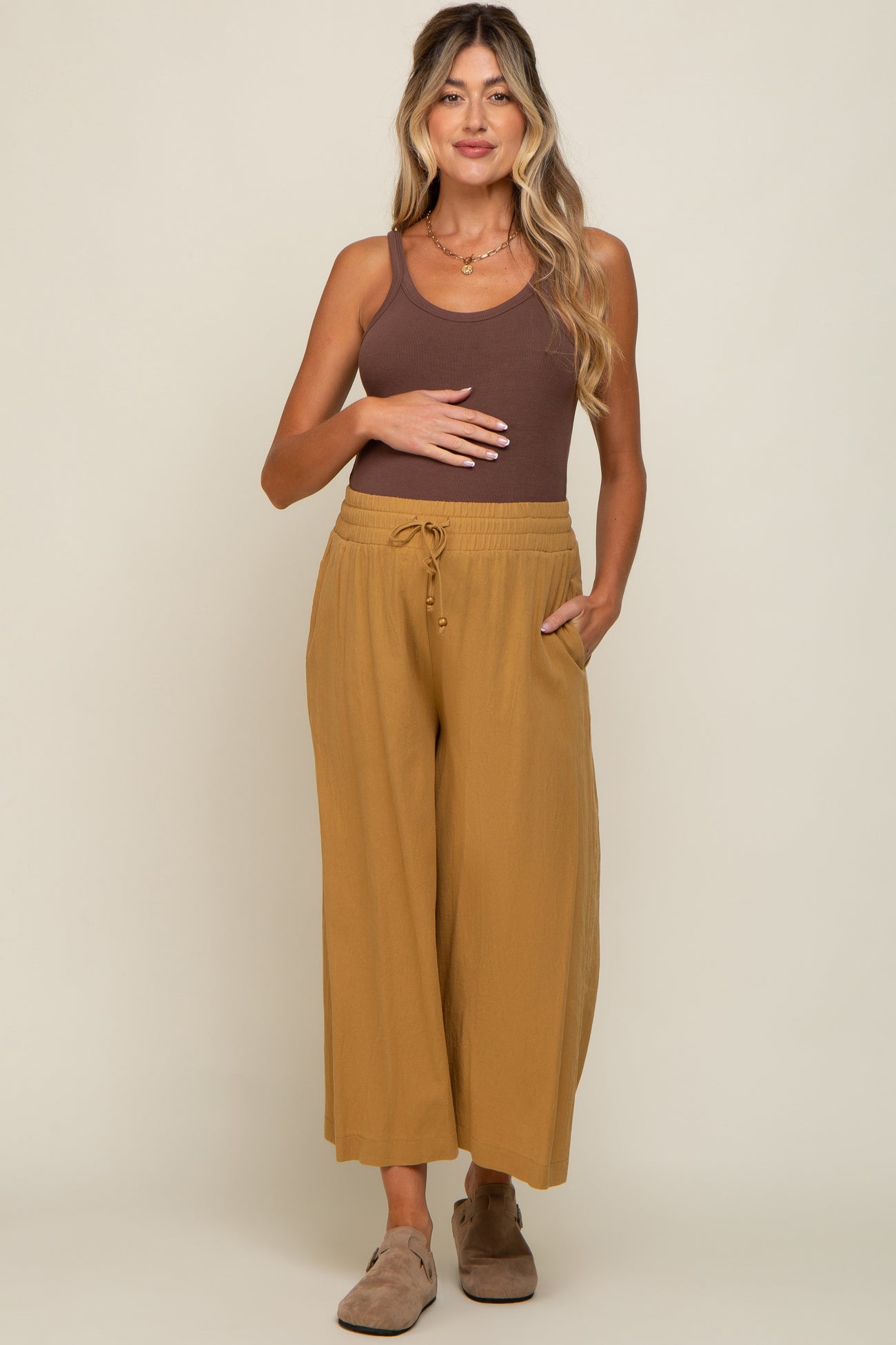 Pregnant woman wearing a brown ribbed tank top and mustard yellow wide-leg maternity pants with a drawstring waist