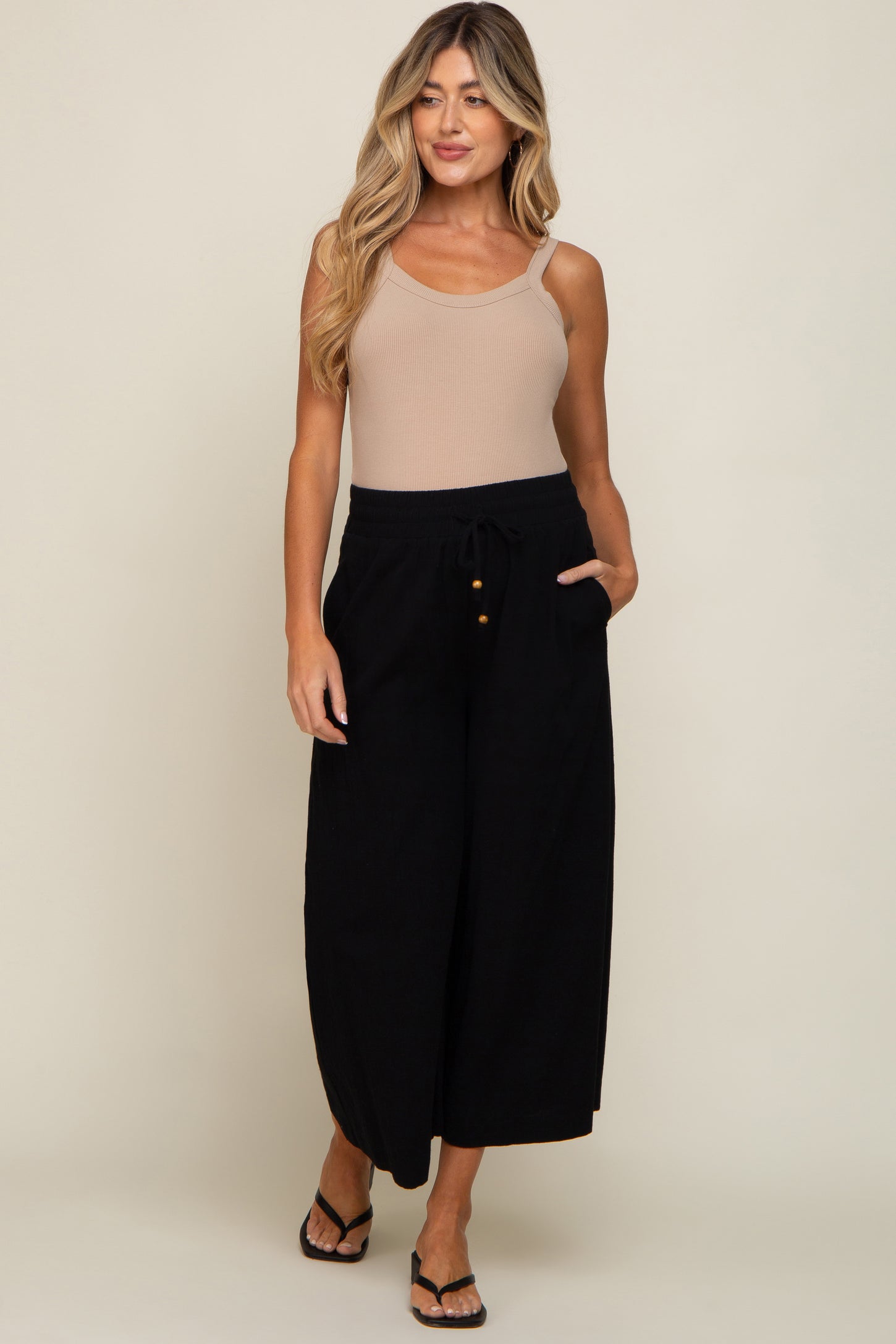 woman wearing a beige ribbed tank top and black wide leg drawstring pants with gold buttons