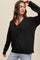 woman wearing a black v-neck ribbed knit sweater and light wash jeans against a neutral background