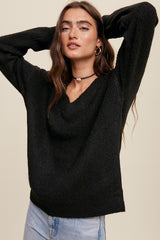woman wearing a black v-neck knit sweater and light wash jeans against a neutral background