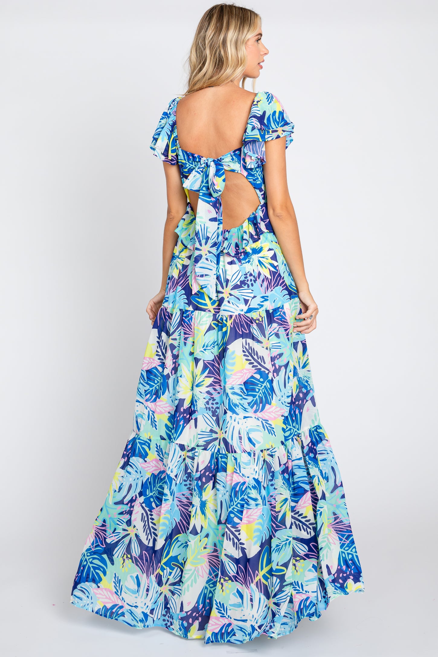 Woman wearing a blue tropical floral print maxi dress with a tie-back cutout and tiered skirt