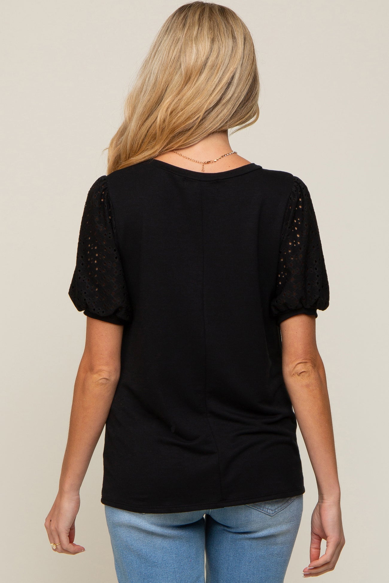 Back view of a woman wearing a black short sleeve top with eyelet puff sleeves and light wash jeans