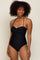 woman with curly hair wearing a black one-piece swimsuit with ruched detailing and halter straps
