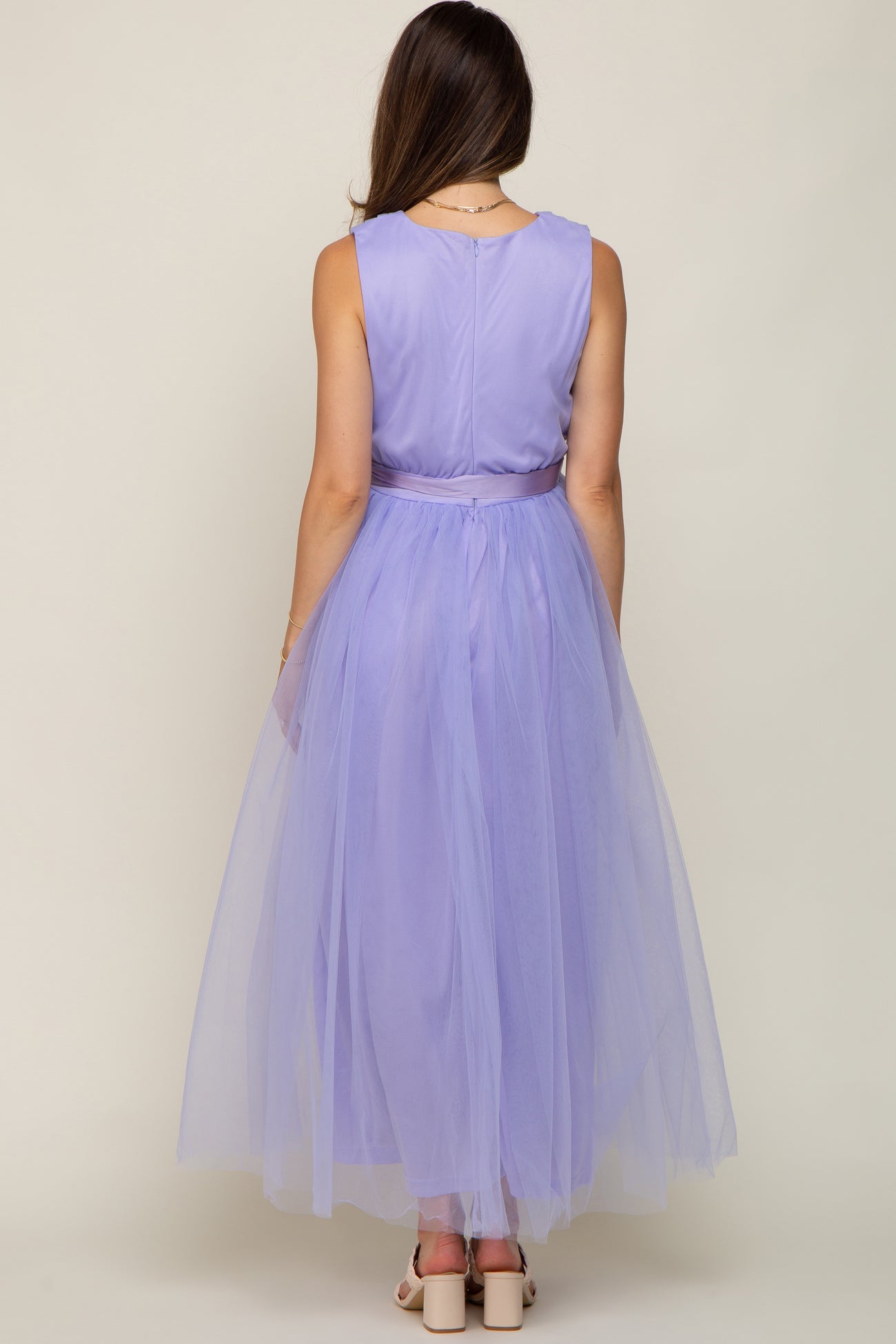 Back view of a woman wearing a sleeveless lavender maxi dress with a tulle skirt and satin waist tie