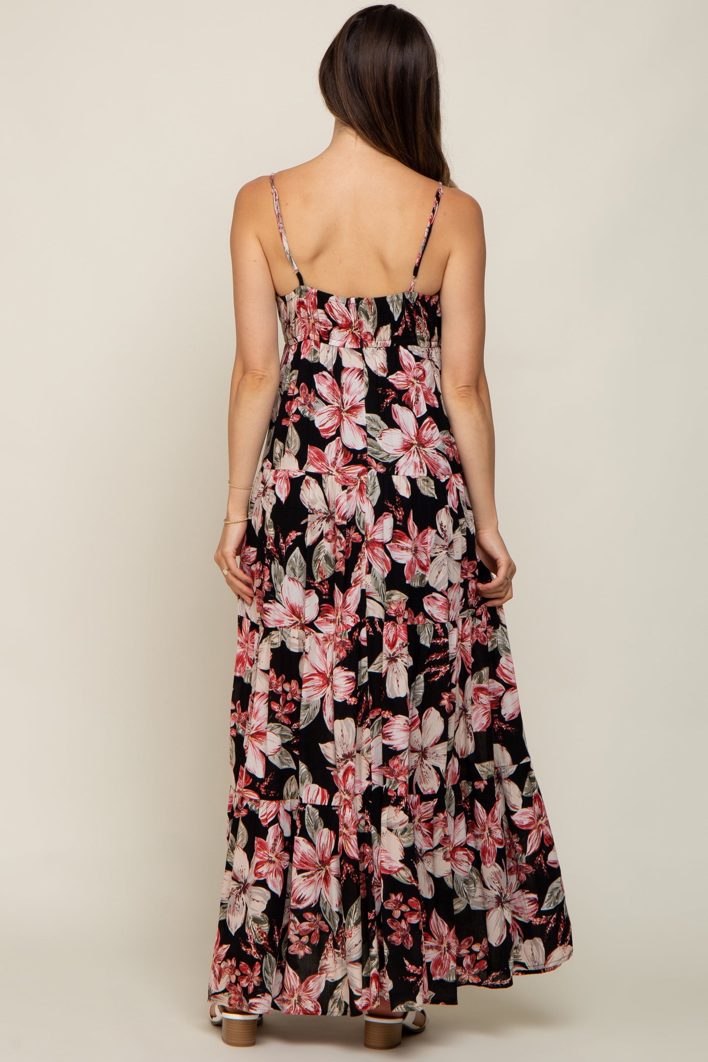 Back view of a woman wearing a black floral tiered maxi dress with pink hibiscus print and spaghetti straps