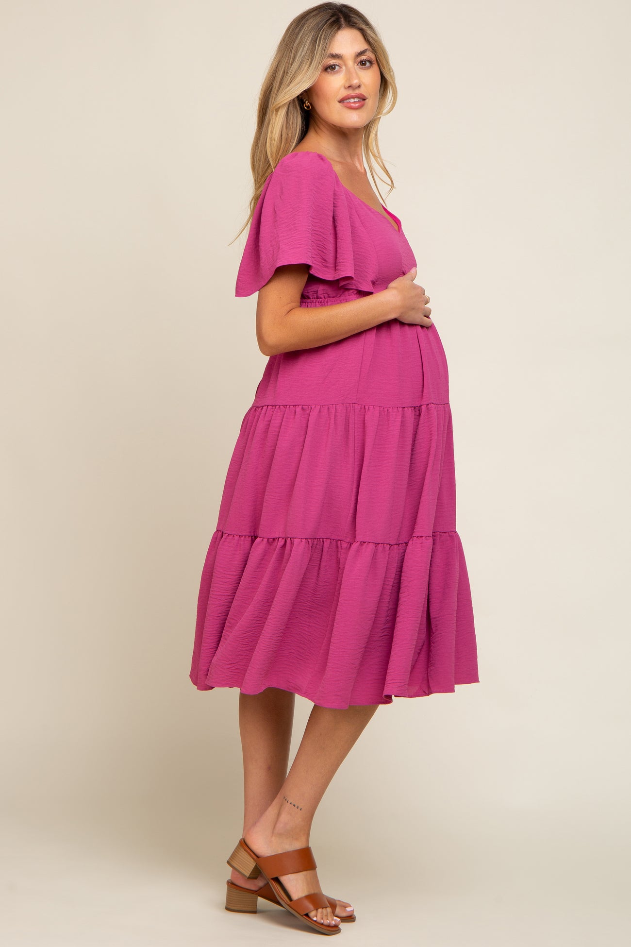 pregnant woman in a magenta tiered maternity dress with flutter sleeves and brown sandals