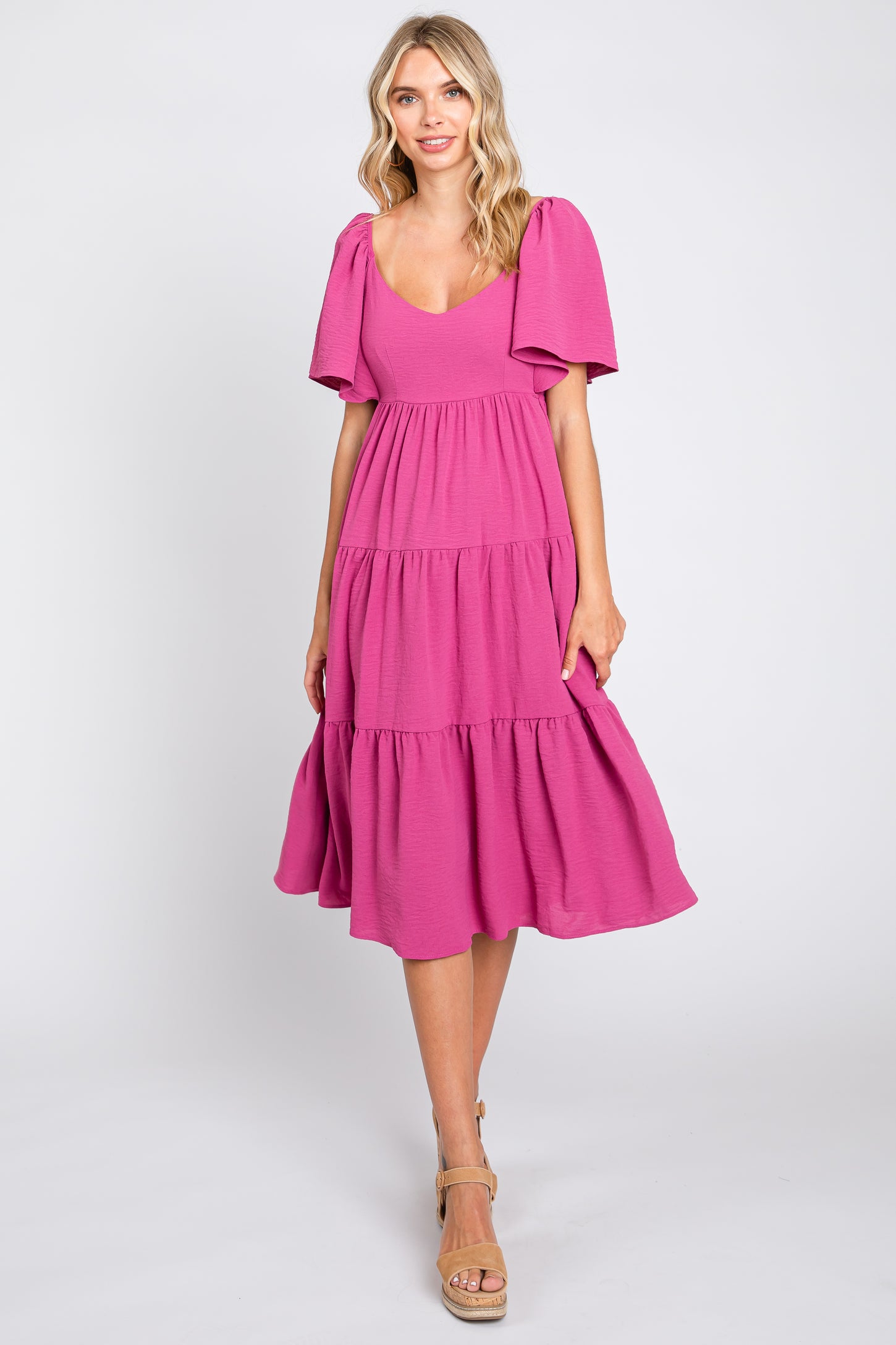 Blonde woman wearing a magenta tiered midi dress with flutter sleeves and tan platform sandals