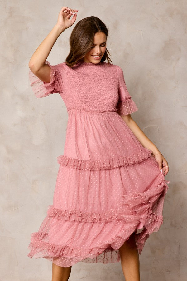 woman wearing a pink dotted midi dress with smocked bodice and ruffled tiered skirt, twirling with a joyful expression
