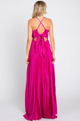 Back view of a woman wearing a hot pink pleated maxi dress with a tie-back detail and crisscross straps.
