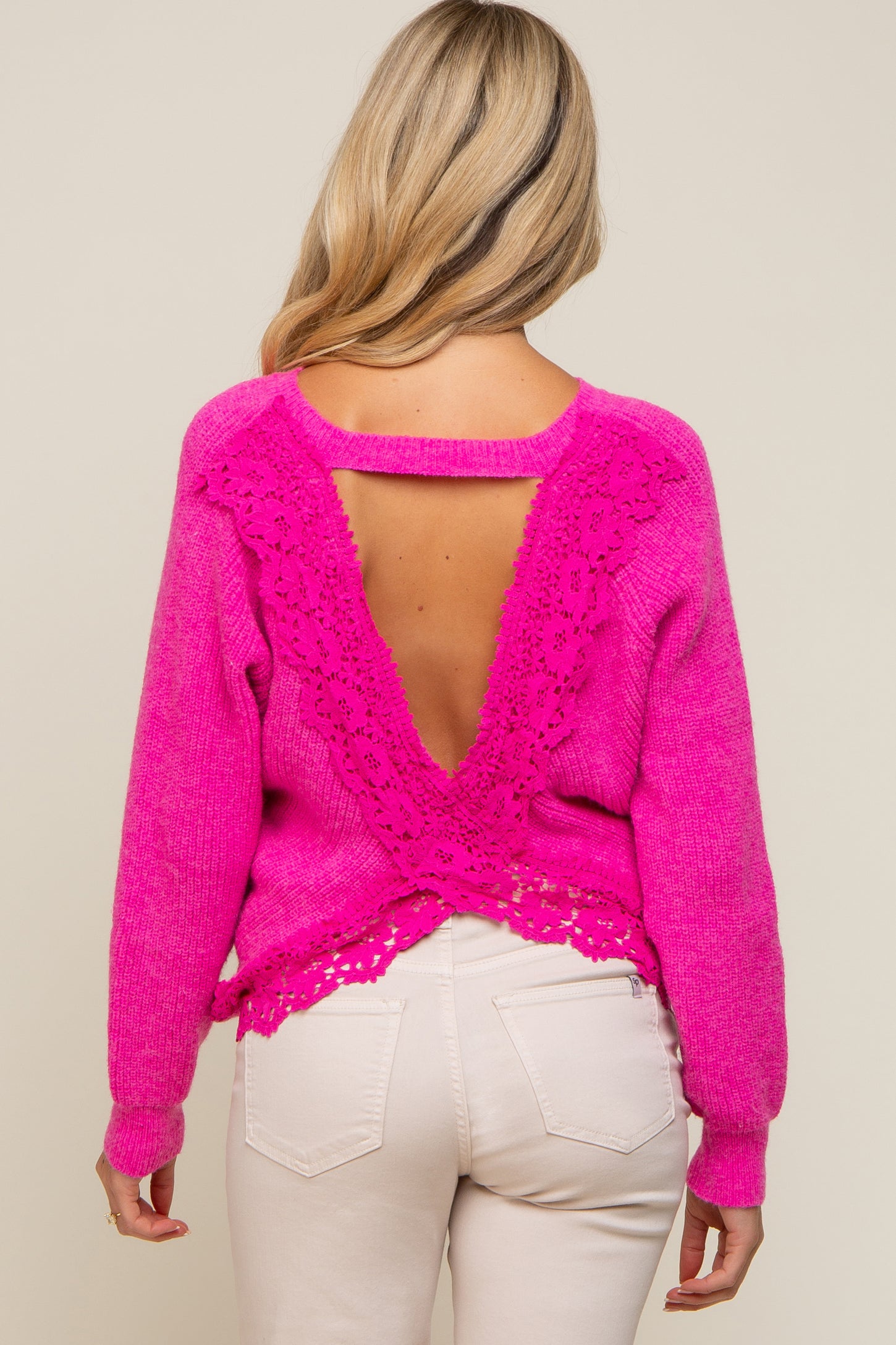 Back view of a woman wearing a hot pink knit sweater with a lace-trimmed open back and white pants