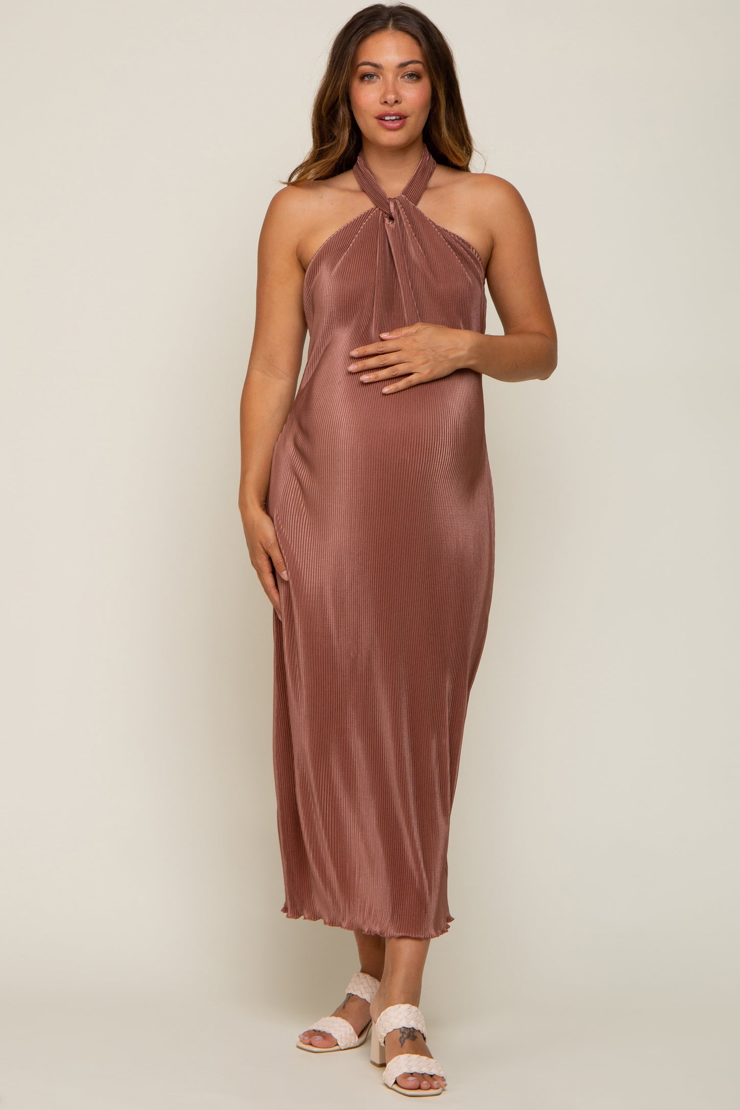 Pregnant woman wearing a mauve pleated halter neck maternity midi dress and white woven heels