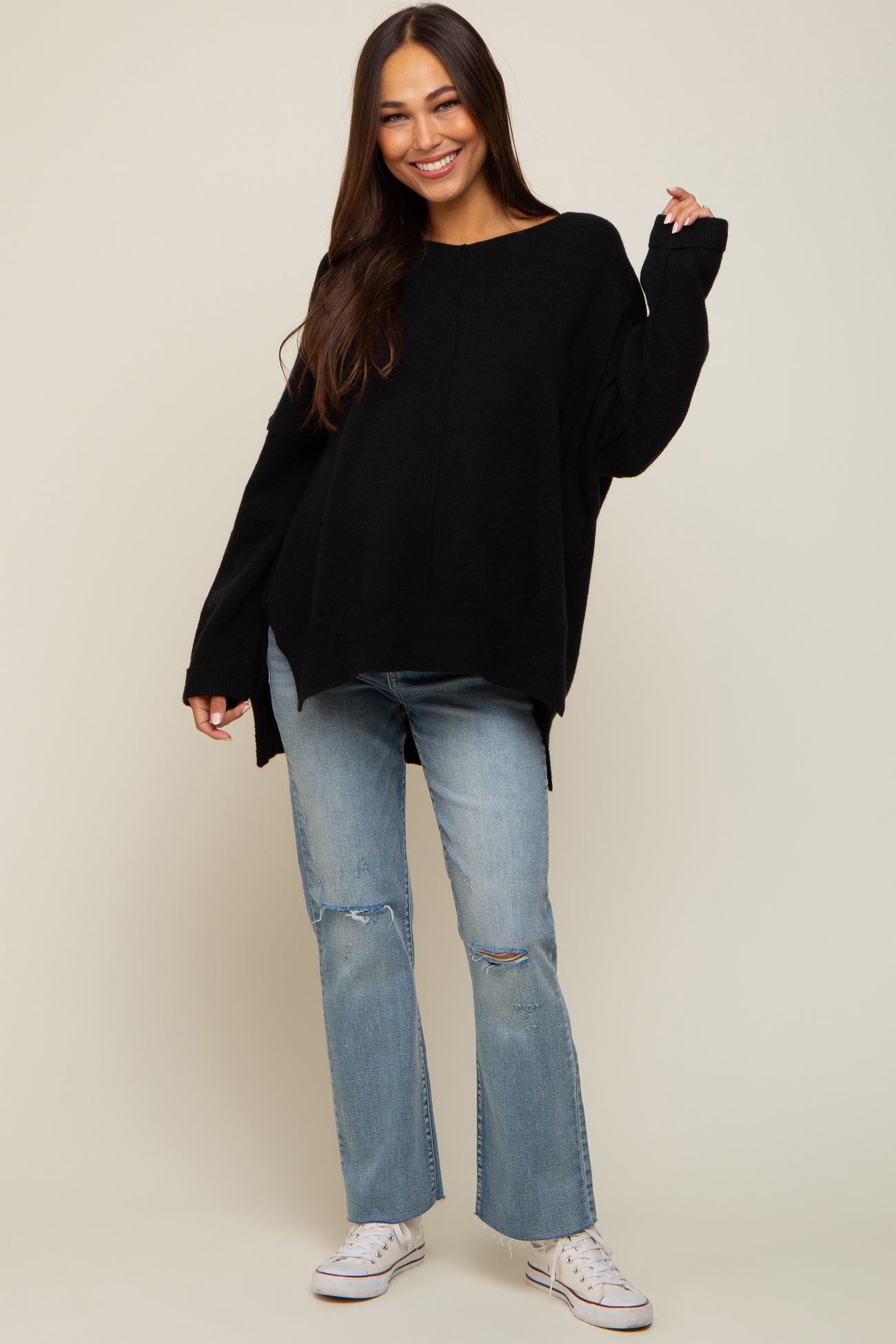 Woman wearing a black oversized knit sweater and distressed light wash jeans with white sneakers