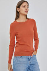 woman wearing a long-sleeved burnt orange crewneck sweater and light wash denim jeans