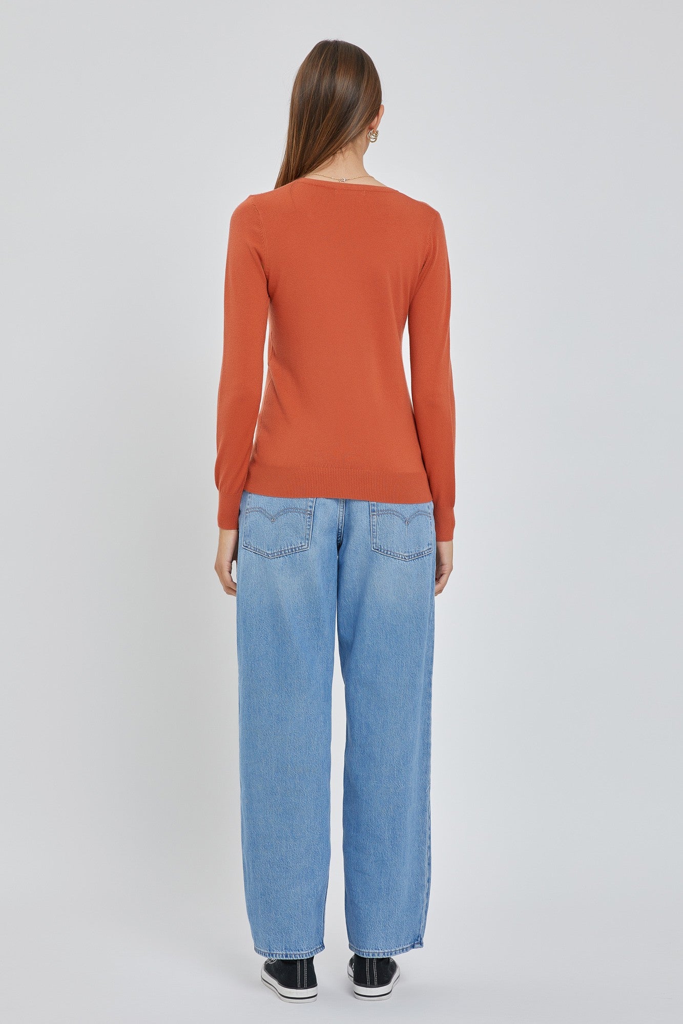 Back view of a woman wearing a long-sleeved burnt orange sweater and light wash wide-leg jeans