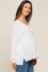 pregnant woman wearing a white v-neck maternity sweater and blue jeans against a neutral background
