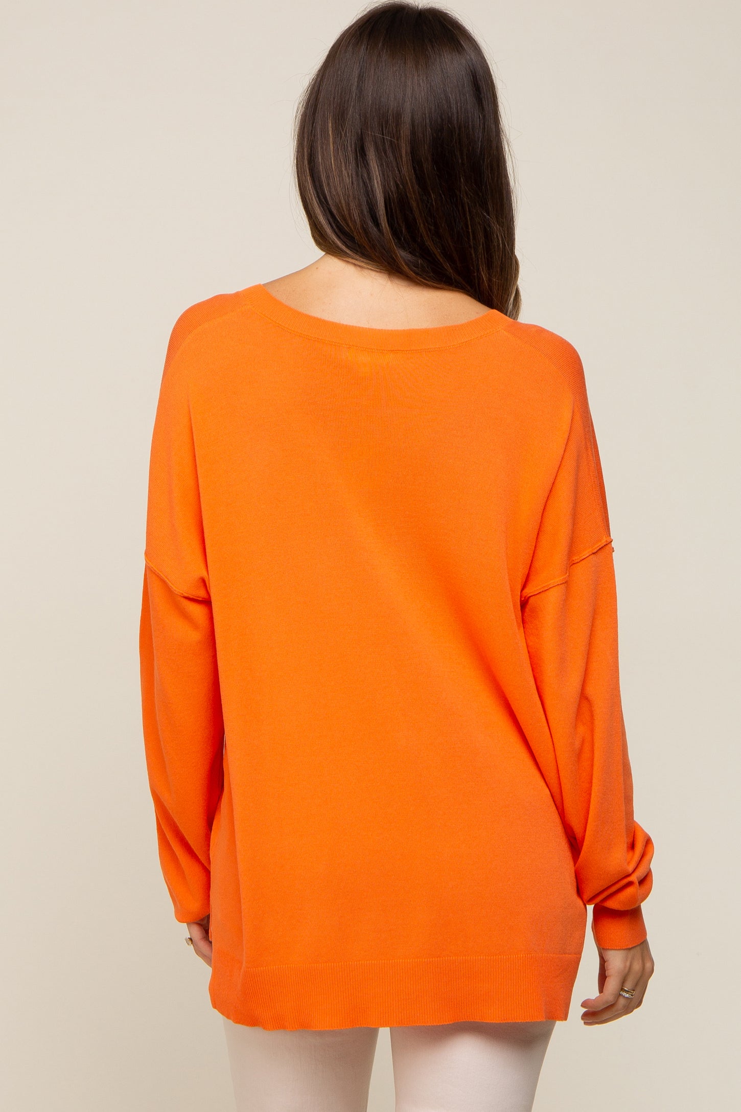 back view of a woman wearing a bright orange oversized long sleeve sweater with drop shoulders