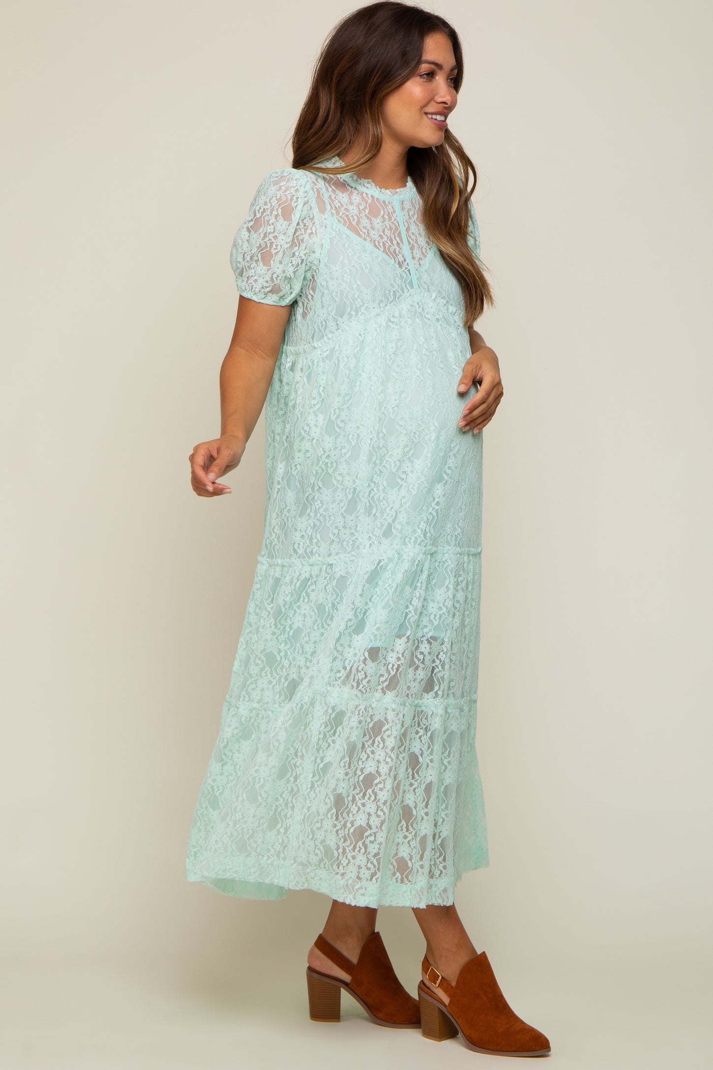 woman wearing a mint green lace maternity dress with puff sleeves and a tiered skirt, showcasing her baby bump