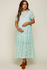 woman wearing a mint green lace maternity dress with short sleeves and a tiered skirt, cradling her baby bump