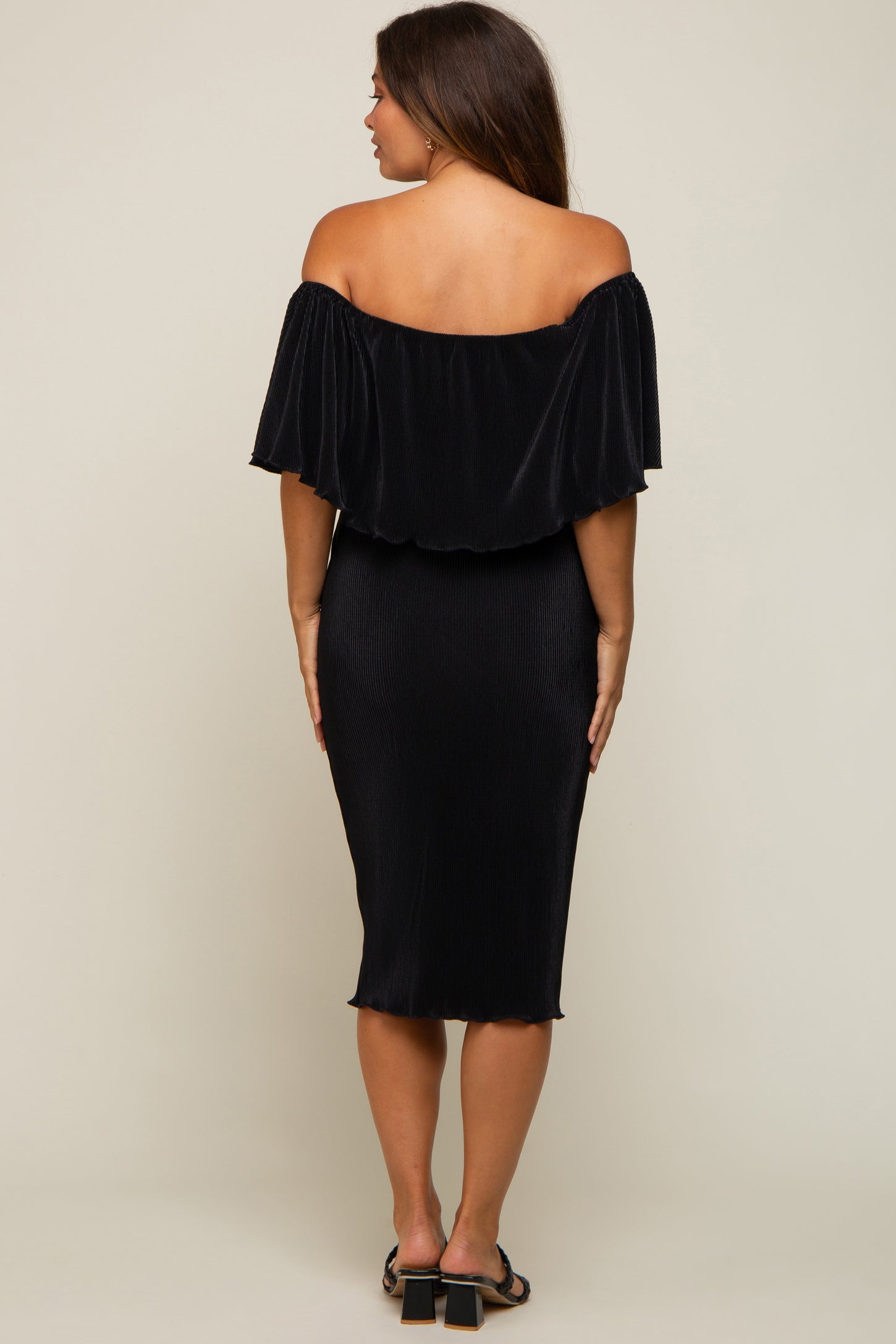 back view of woman wearing black off the shoulder pleated midi dress with ruffle overlay