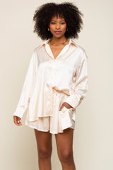 Woman wearing cream satin button-down shirt and matching shorts lounge set with gold chain necklace