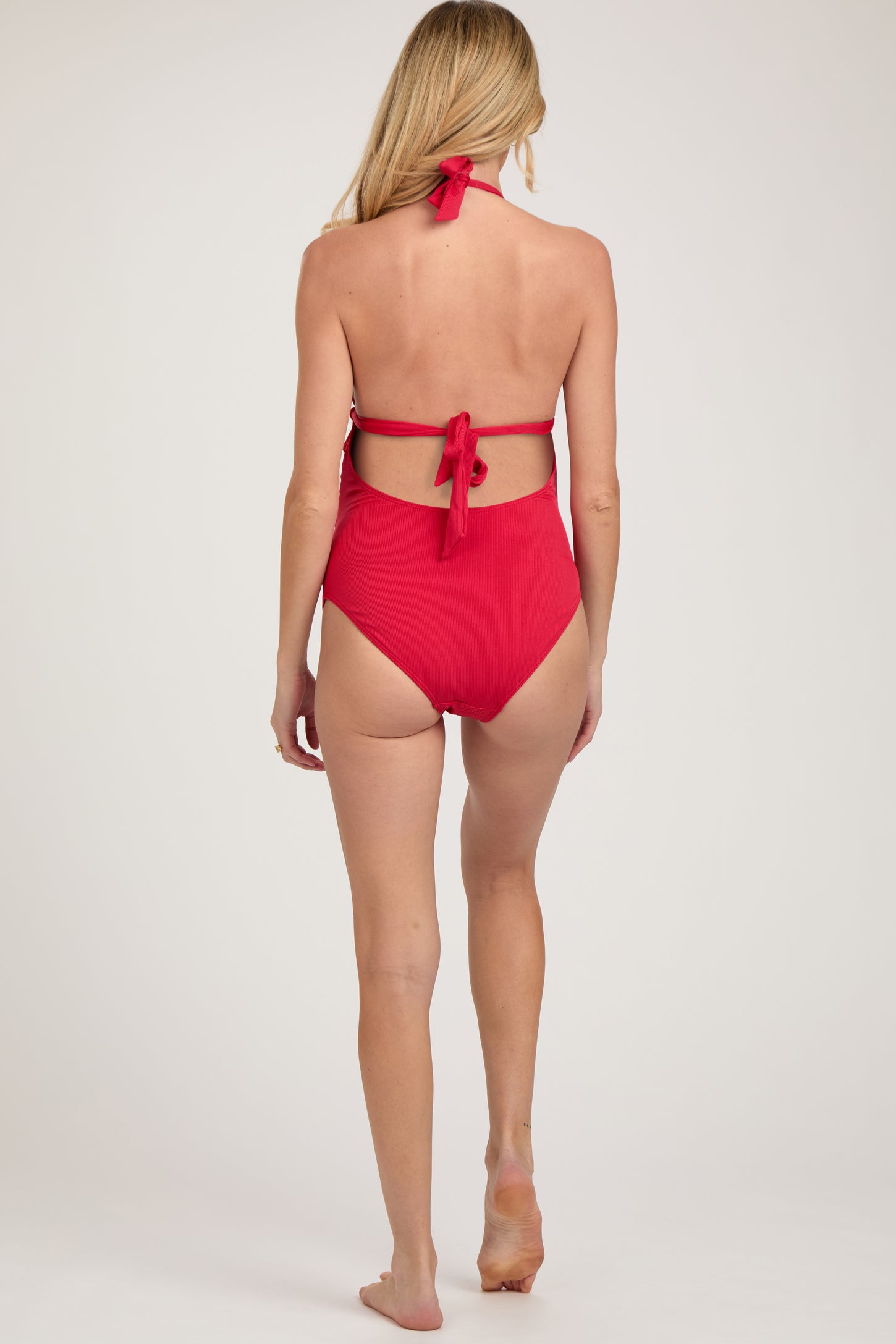 woman wearing a red maternity swimsuit with a halter neck and open back, showing a baby bump