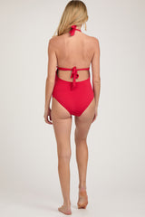 woman wearing a red maternity swimsuit with a halter neck and open back, showing a baby bump