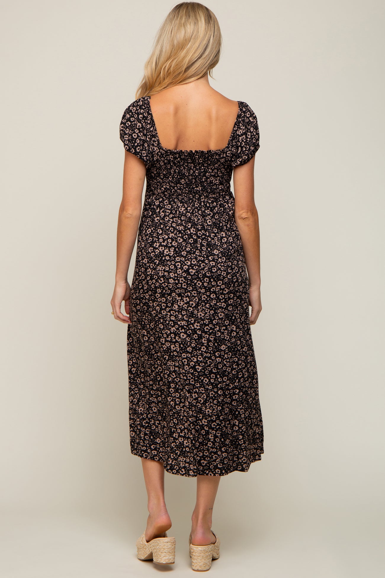 Back view of a woman wearing a black floral smocked midi dress with puff sleeves and tan wedge sandals