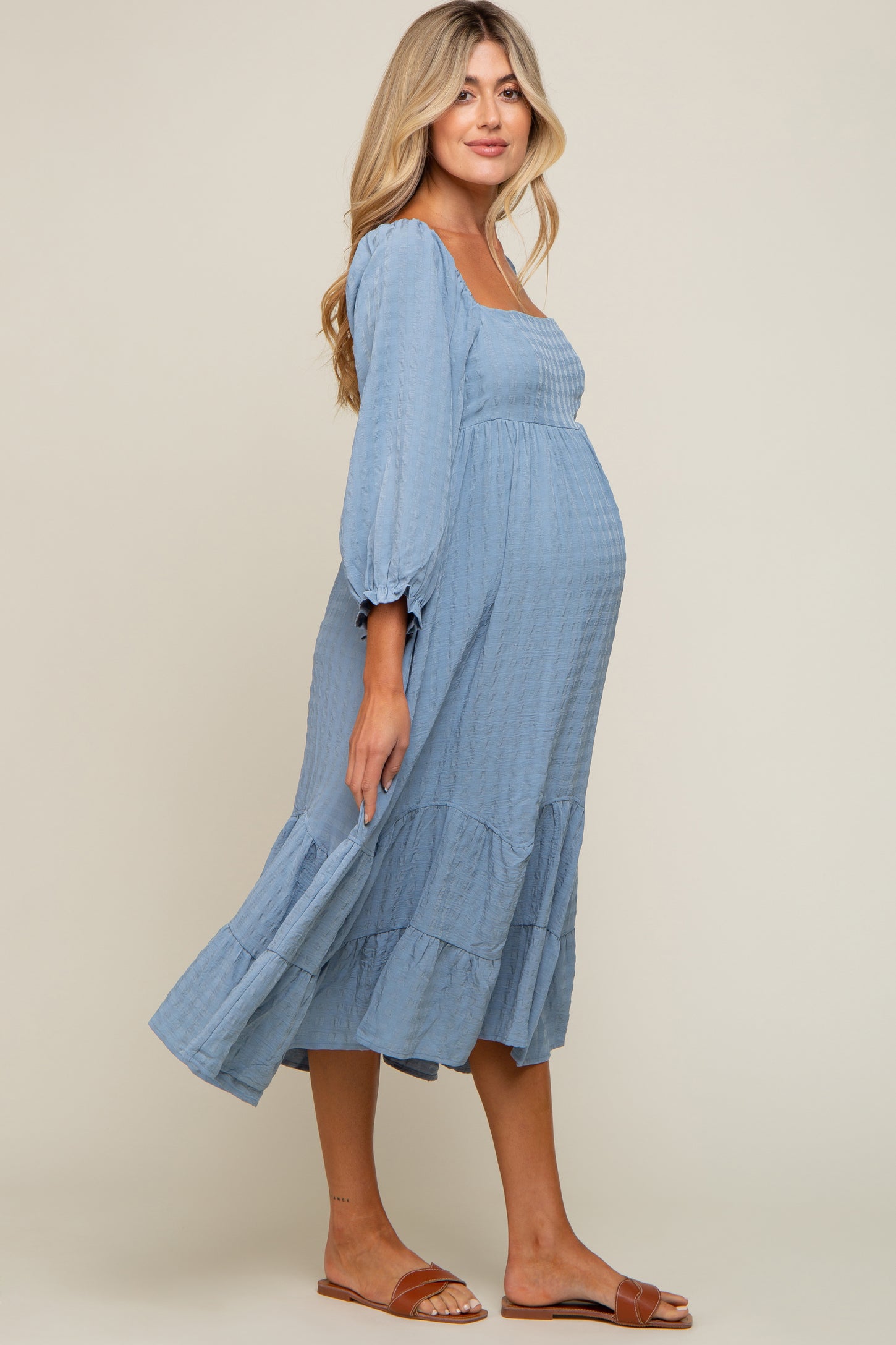 Pregnant woman wearing a light blue long sleeve maternity midi dress with tiered skirt and brown sandals