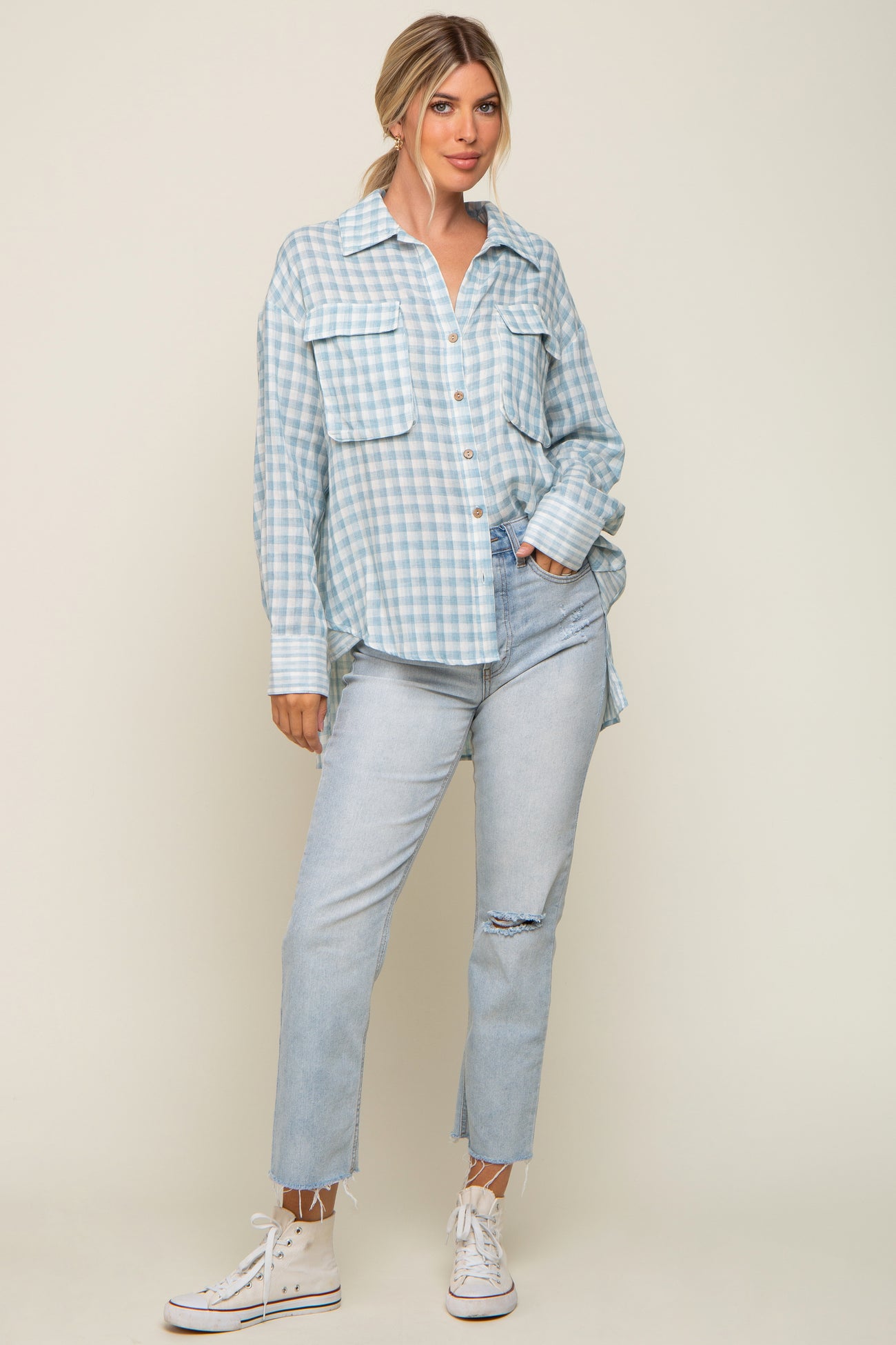 woman wearing light blue gingham button down shirt and distressed denim jeans with white sneakers