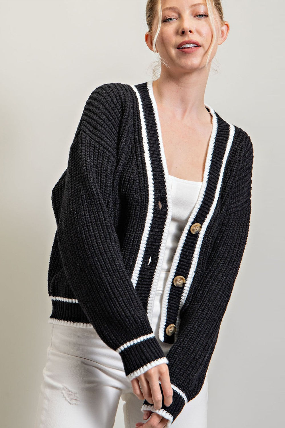 Woman wearing a black chunky knit cardigan with white stripes and brown buttons over a white top