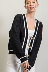 Woman wearing a black chunky knit cardigan with white stripes and brown buttons over a white top