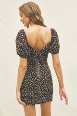 woman wearing a brown floral backless mini dress with puff sleeves and a tying detail at the back
