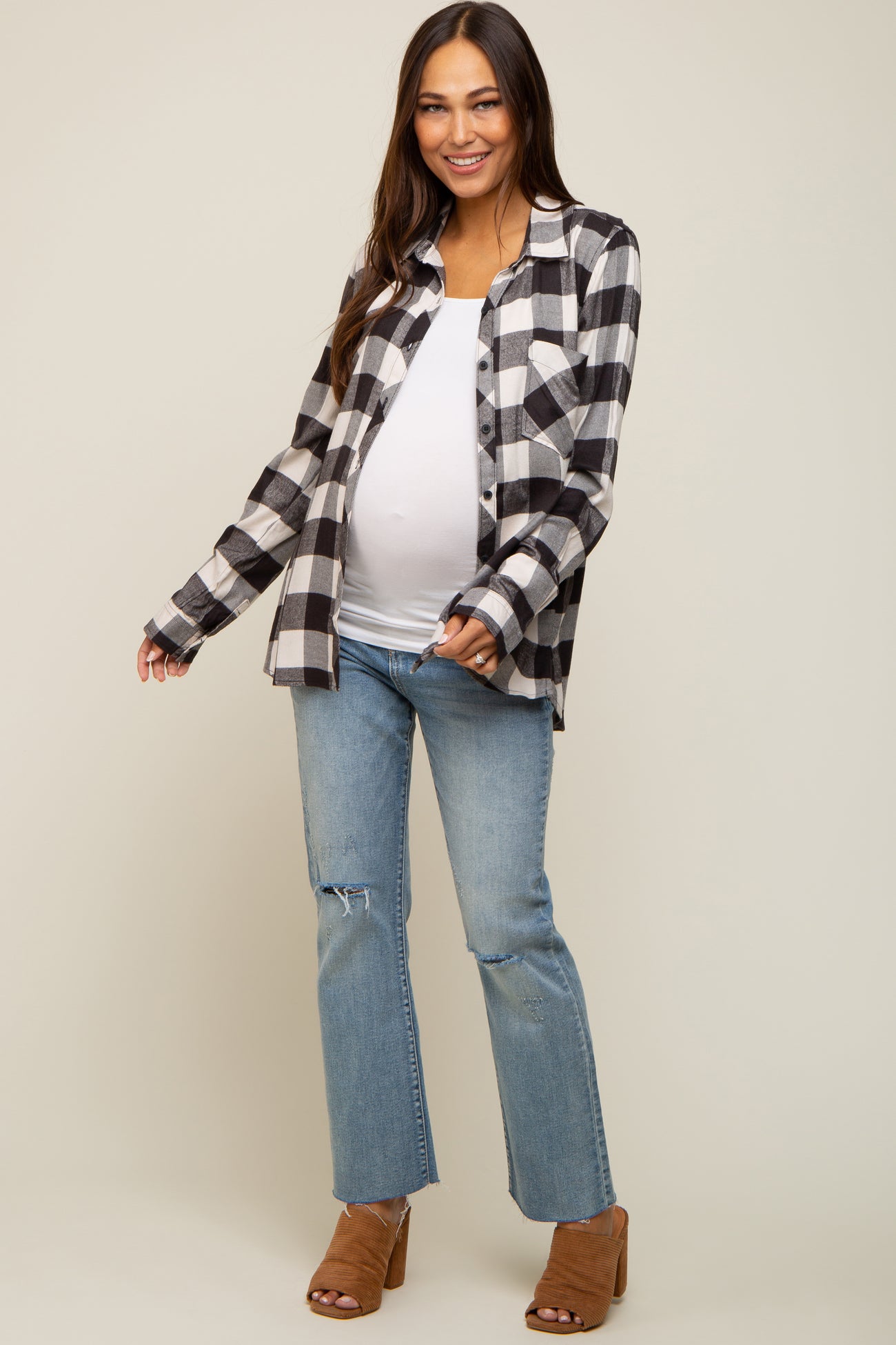 Smiling pregnant woman wearing a black and white plaid maternity shirt with blue jeans and brown heels