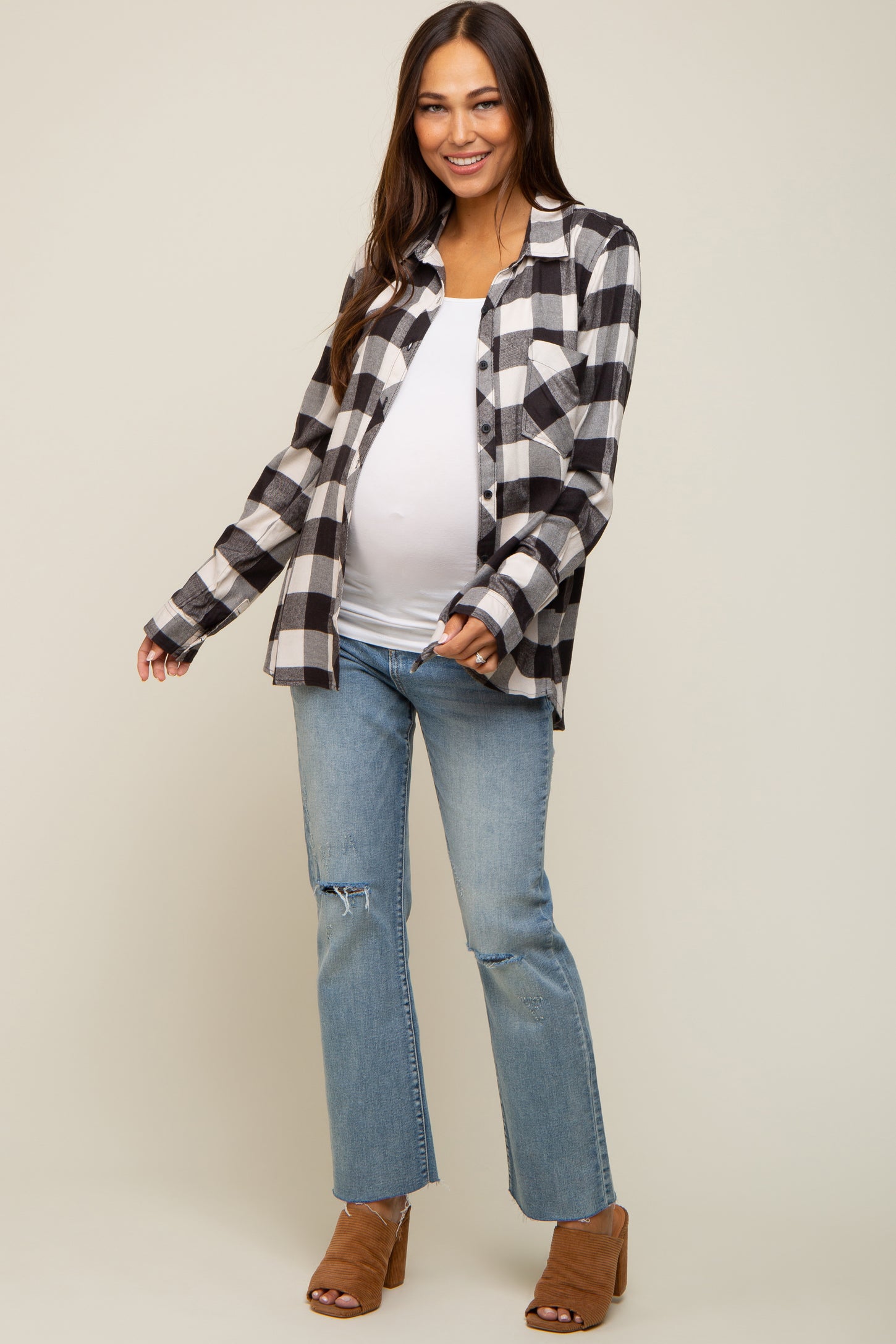 Smiling pregnant woman wearing a black and white plaid maternity shirt with blue jeans and brown heels