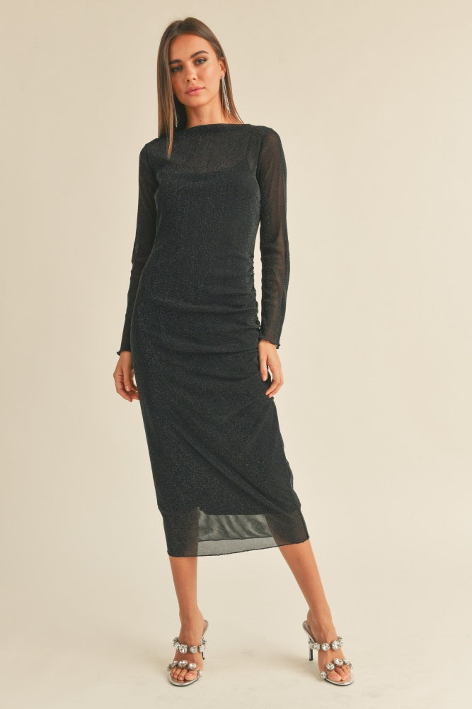 woman wearing a black long sleeve midi dress with ruched detailing and sheer sleeves, standing elegantly against a neutral background