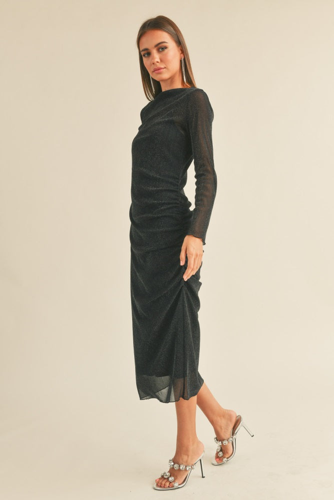 woman wearing a fitted black long sleeve midi dress with ruched details and transparent long sleeves, styled with heels