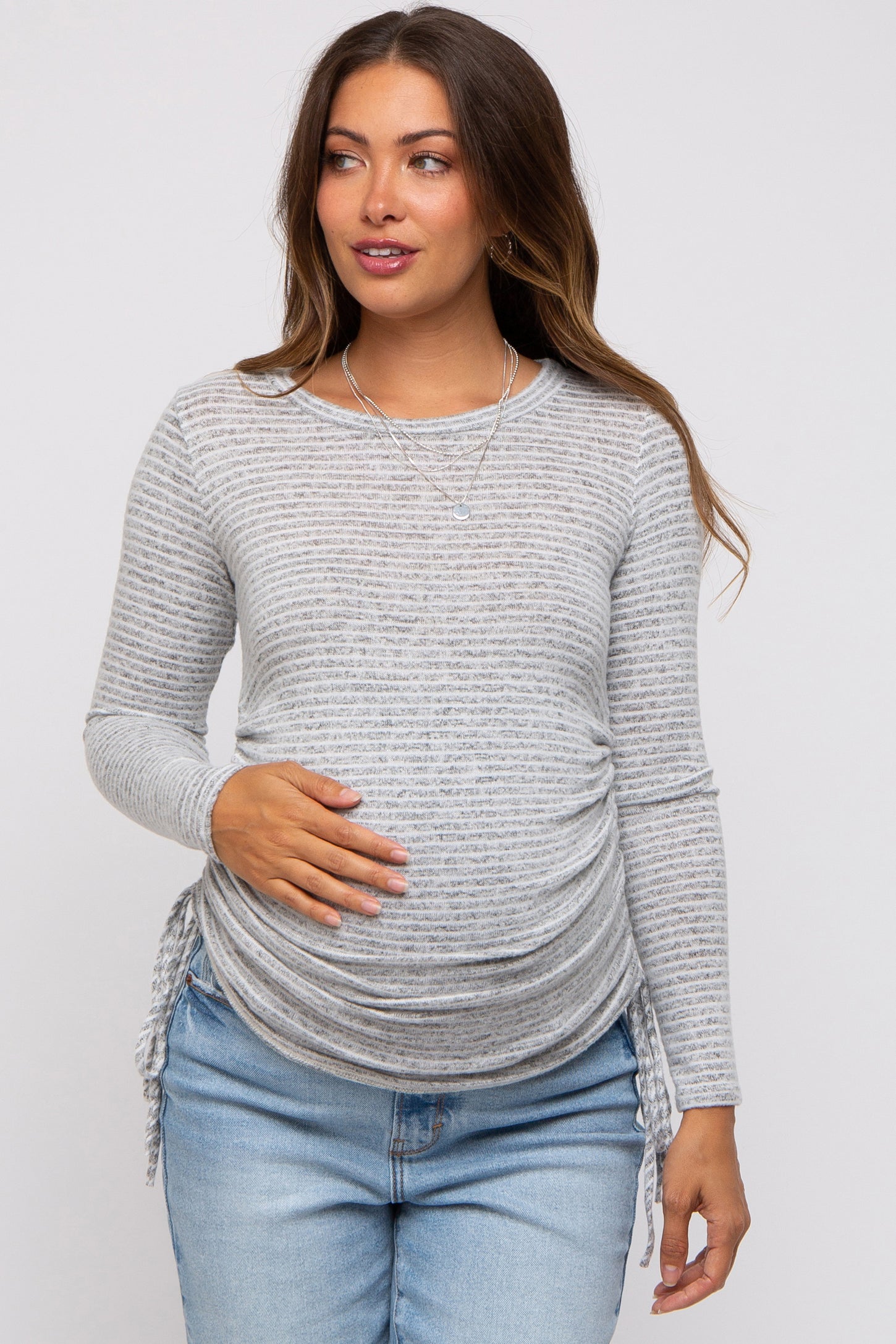 woman wearing a grey striped long sleeve maternity top with side ruching and holding her baby bump