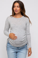 woman wearing a grey striped long sleeve maternity top with side ruching and holding her baby bump
