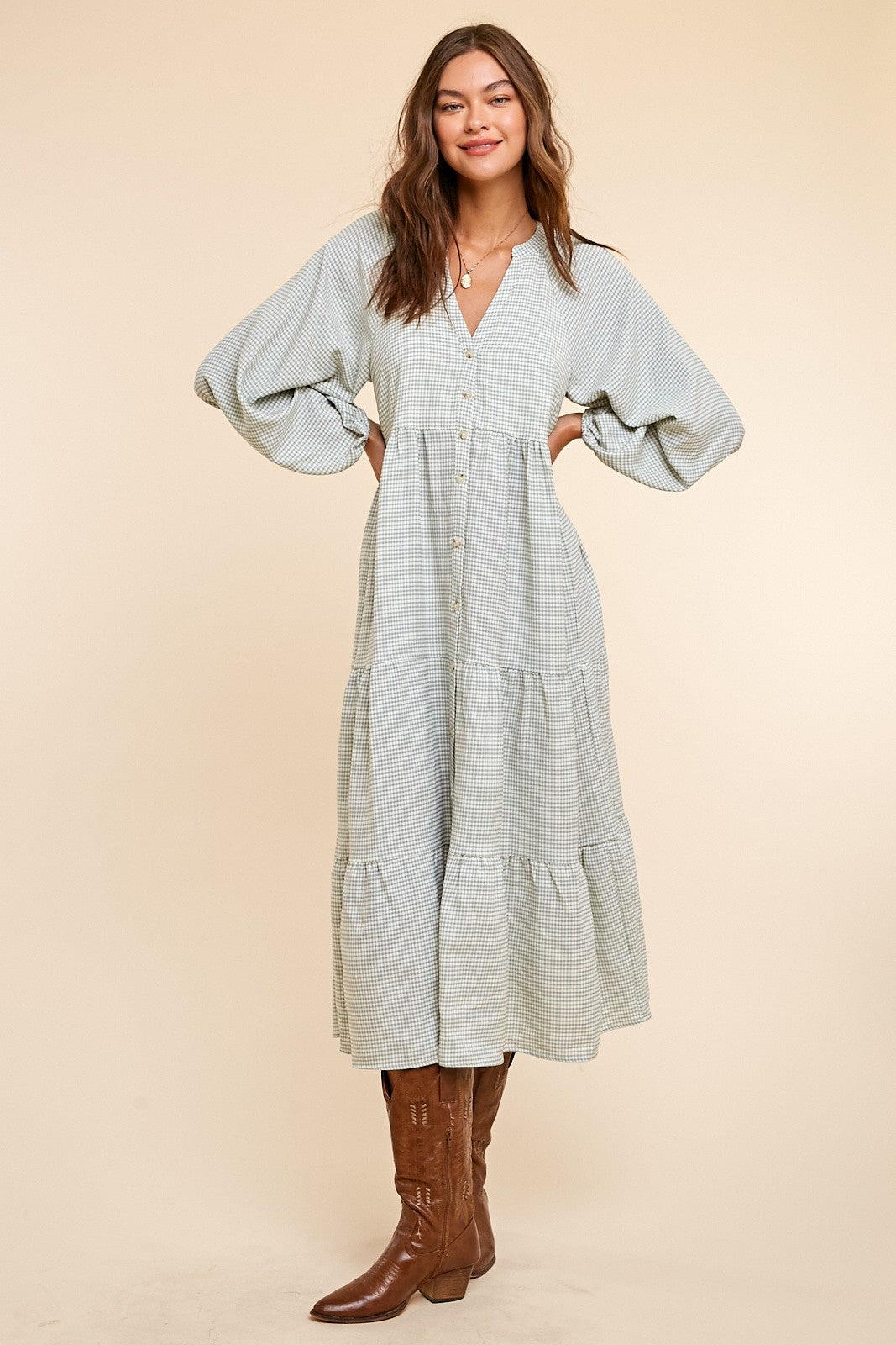 Woman wearing a green and white gingham tiered midi dress with puff sleeves and brown leather cowboy boots